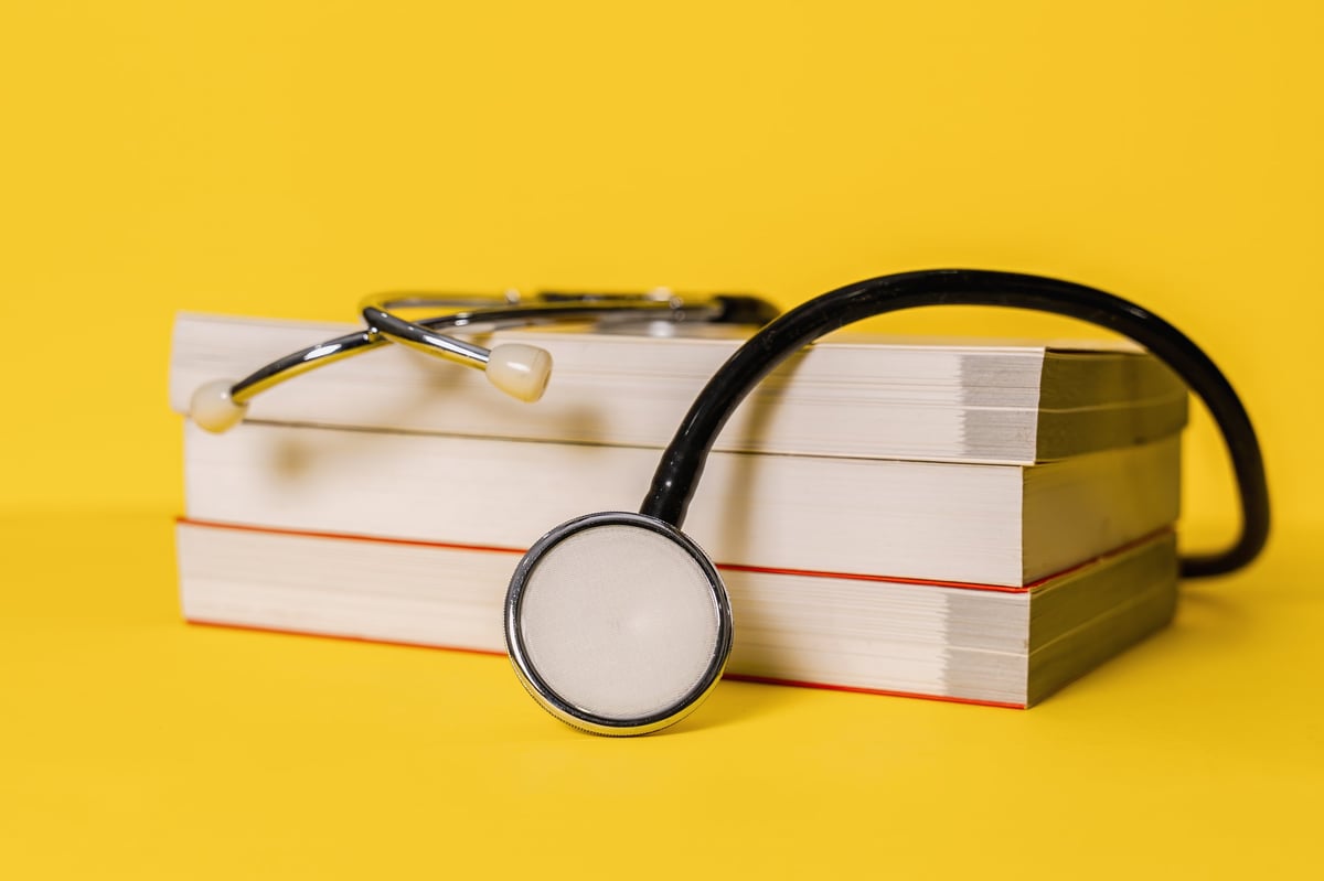 Stethoscope resting on stacked medical textbooks against a bright yellow background